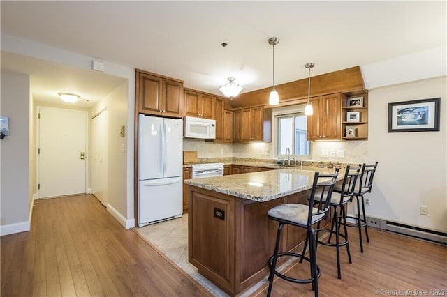 kitchen with light hardwood / wood-style floors, kitchen peninsula, white appliances, light stone countertops, and pendant lighting