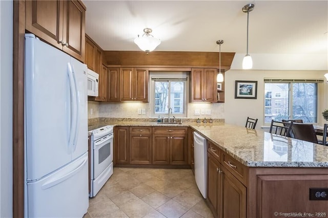 kitchen with decorative light fixtures, kitchen peninsula, sink, white appliances, and light stone counters