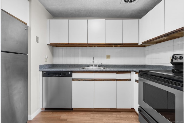 kitchen with tasteful backsplash, sink, white cabinetry, light hardwood / wood-style flooring, and appliances with stainless steel finishes