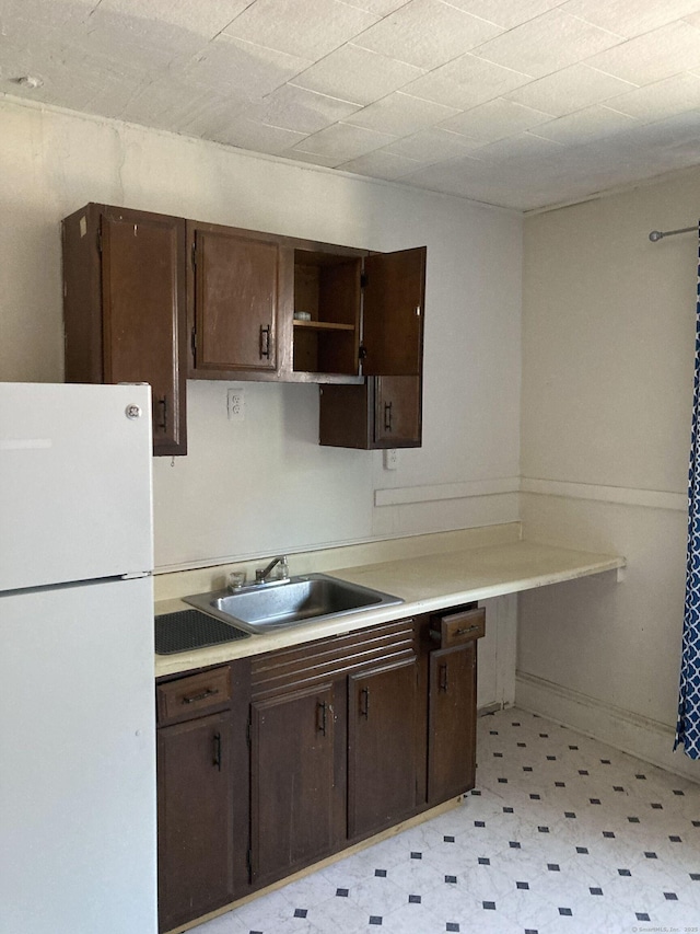 kitchen with dark brown cabinets, sink, and white fridge