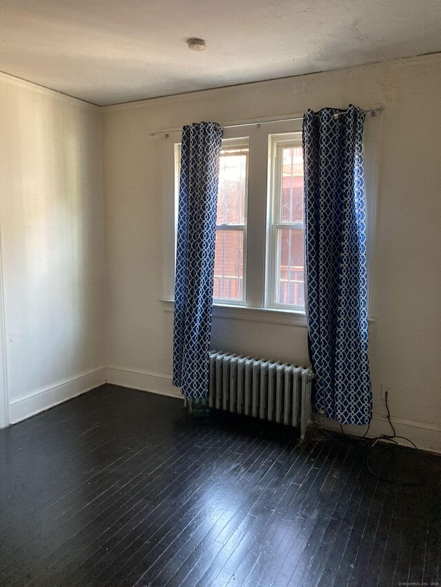 empty room featuring dark wood-type flooring and radiator heating unit