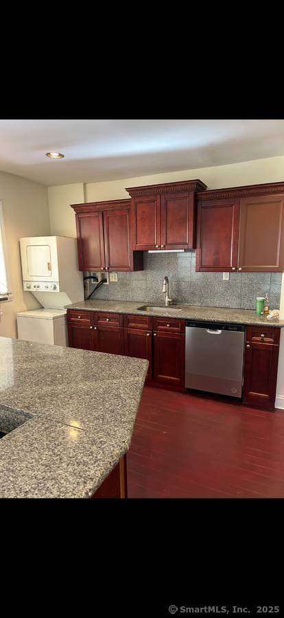 kitchen with tasteful backsplash, dishwasher, sink, stacked washer / drying machine, and light stone countertops