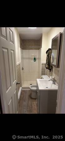 bathroom featuring tiled shower, vanity, toilet, and tile walls