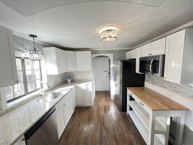 kitchen featuring white cabinetry, butcher block countertops, stainless steel appliances, decorative light fixtures, and sink