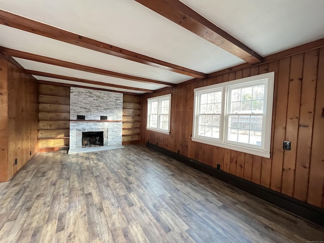 unfurnished living room with dark hardwood / wood-style floors, wood walls, beam ceiling, built in features, and a stone fireplace