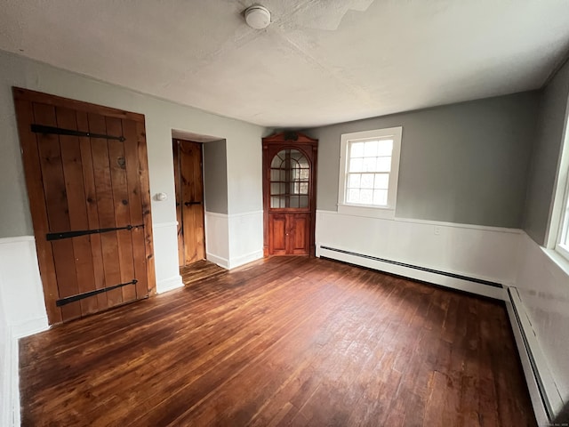 spare room featuring a baseboard heating unit and dark hardwood / wood-style floors