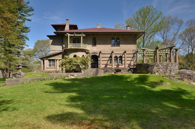 view of front of house with a front yard, a chimney, a balcony, and stucco siding