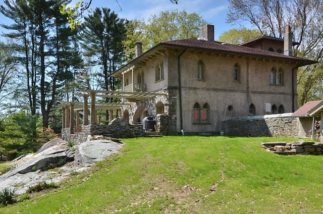 rear view of property featuring a yard, a chimney, stucco siding, and a pergola