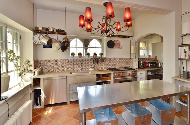 kitchen with stainless steel appliances, stainless steel countertops, a sink, radiator, and tasteful backsplash