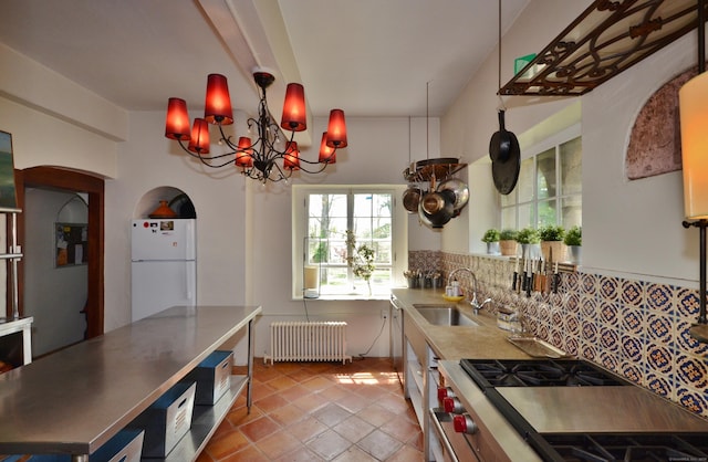 kitchen featuring decorative backsplash, radiator, freestanding refrigerator, stainless steel stove, and a sink