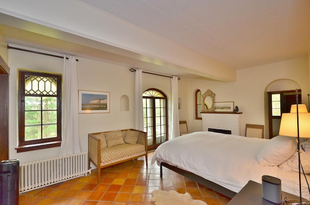 bedroom with multiple windows, radiator heating unit, a brick fireplace, and beamed ceiling