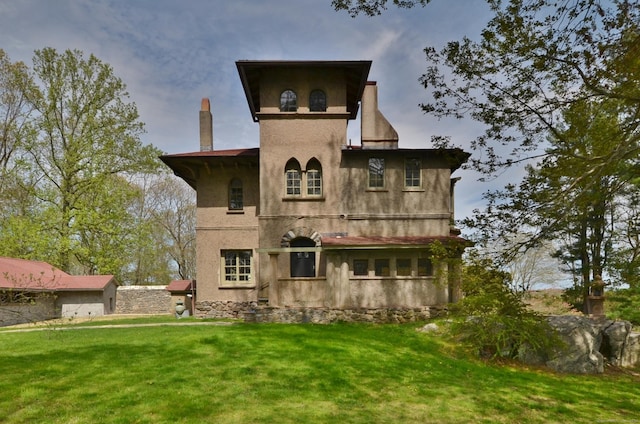 back of property with a yard, a chimney, and stucco siding