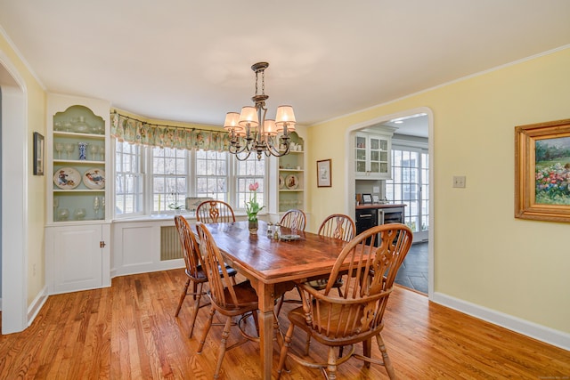 dining space featuring an inviting chandelier, crown molding, built in features, and light wood-type flooring