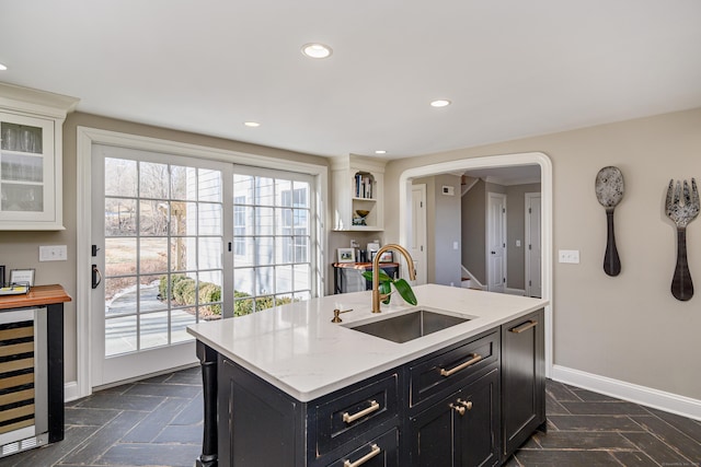 kitchen with white cabinetry, an island with sink, sink, wine cooler, and light stone counters