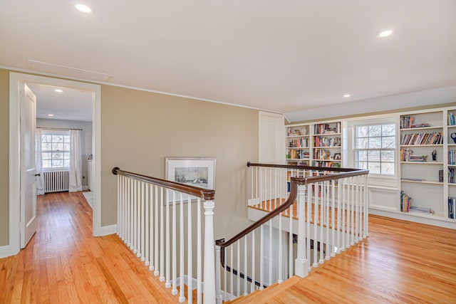 hallway with crown molding, built in shelves, radiator heating unit, and light hardwood / wood-style floors