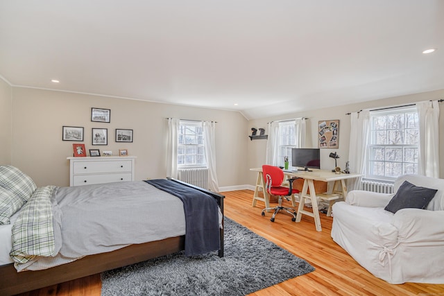 bedroom featuring hardwood / wood-style flooring, lofted ceiling, radiator, and multiple windows