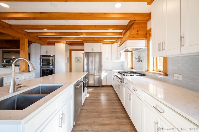 kitchen featuring appliances with stainless steel finishes, a sink, premium range hood, white cabinetry, and beam ceiling