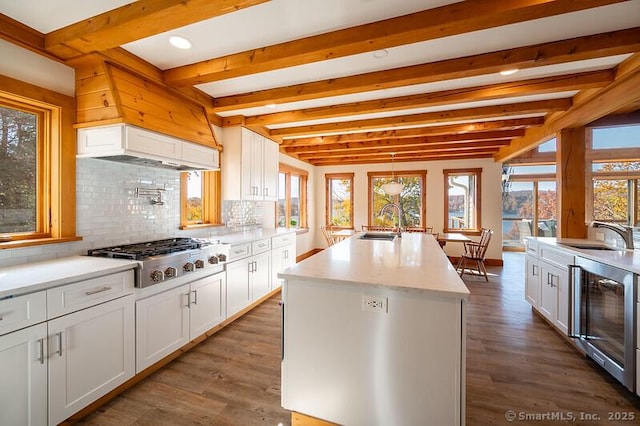 kitchen featuring wine cooler, stainless steel gas cooktop, white cabinets, a kitchen island with sink, and backsplash