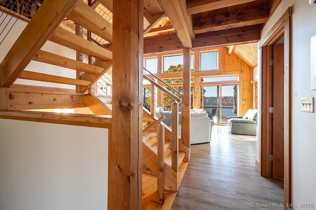 corridor featuring a water view, vaulted ceiling with beams, wood walls, and light wood finished floors