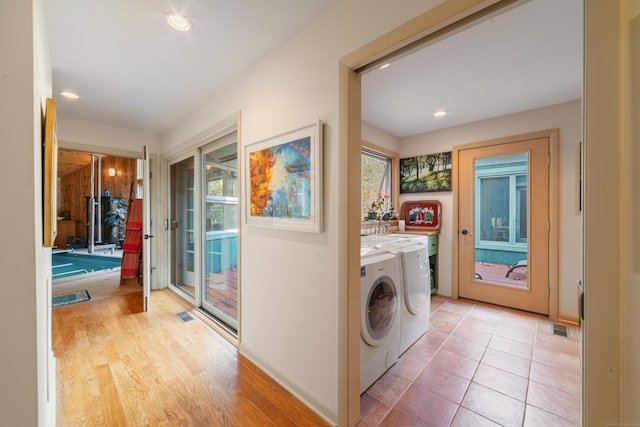 clothes washing area with light wood-type flooring, a healthy amount of sunlight, and washing machine and dryer