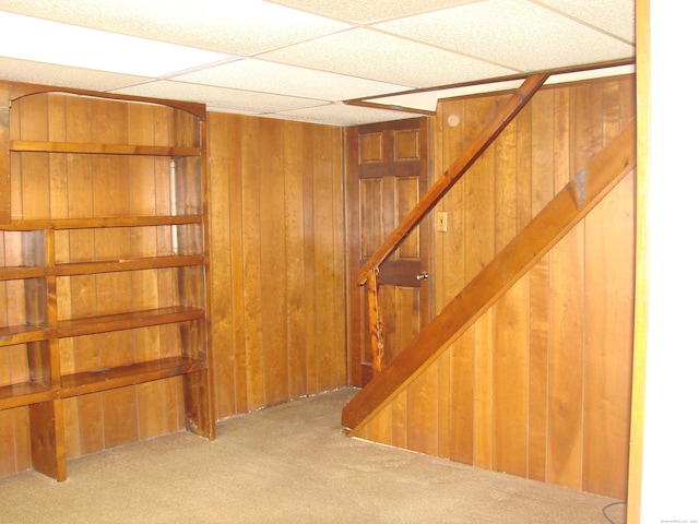 basement with carpet floors, a drop ceiling, and wood walls