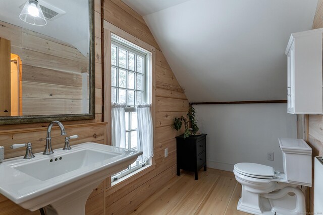 bathroom featuring toilet, vaulted ceiling, wood walls, hardwood / wood-style floors, and sink