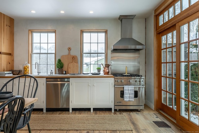 kitchen featuring sink, light wood-type flooring, appliances with stainless steel finishes, white cabinets, and wall chimney exhaust hood