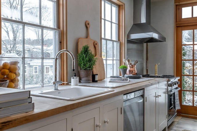 kitchen featuring white cabinets, sink, appliances with stainless steel finishes, and wall chimney range hood