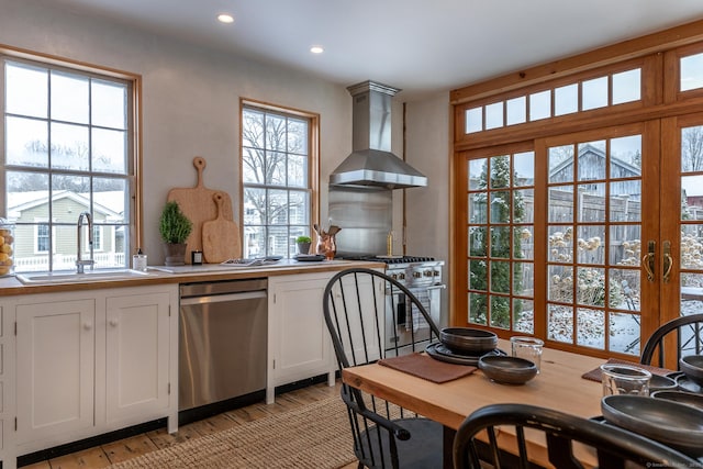 kitchen with wall chimney range hood, sink, white cabinetry, light hardwood / wood-style flooring, and appliances with stainless steel finishes