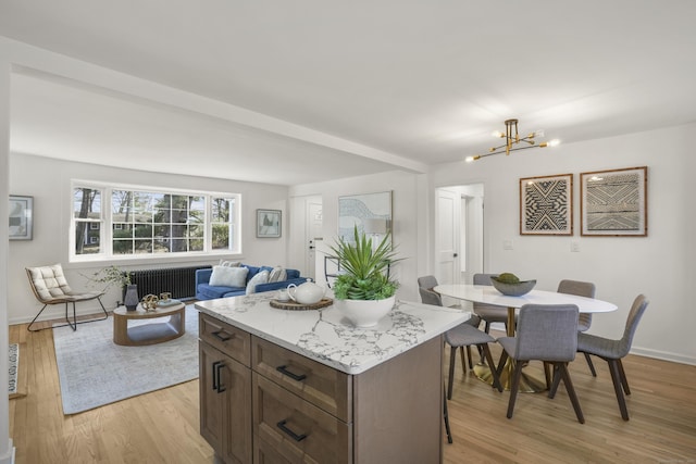 kitchen with a center island, light hardwood / wood-style floors, an inviting chandelier, light stone countertops, and radiator heating unit