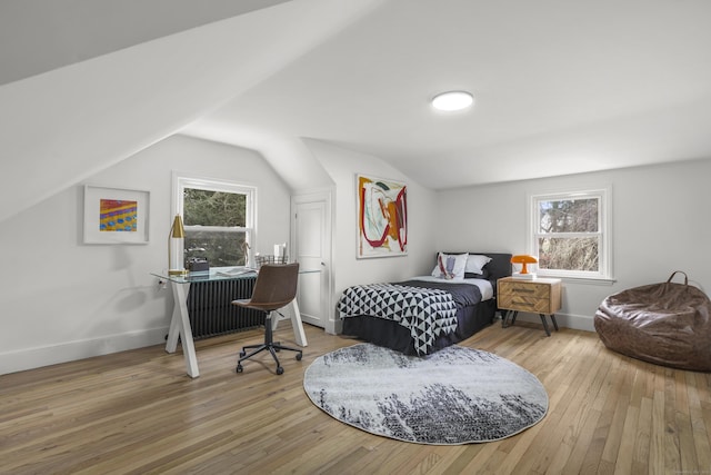 bedroom featuring lofted ceiling, radiator, multiple windows, and hardwood / wood-style flooring