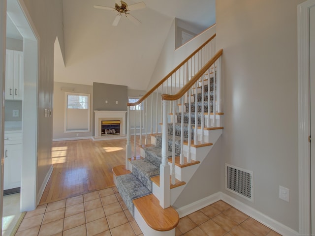 stairs with ceiling fan, tile patterned floors, and high vaulted ceiling