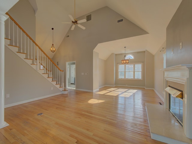 unfurnished living room featuring a high ceiling, a premium fireplace, ceiling fan with notable chandelier, and light hardwood / wood-style floors