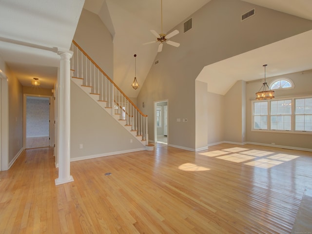 unfurnished living room featuring a high ceiling, ceiling fan with notable chandelier, ornate columns, and light hardwood / wood-style floors