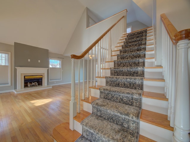 stairs with high vaulted ceiling, a healthy amount of sunlight, and hardwood / wood-style floors