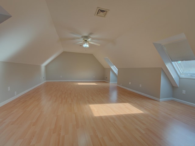 additional living space featuring ceiling fan, vaulted ceiling with skylight, and light hardwood / wood-style flooring