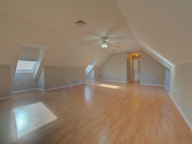 bonus room featuring light wood-type flooring, ceiling fan, and vaulted ceiling with skylight