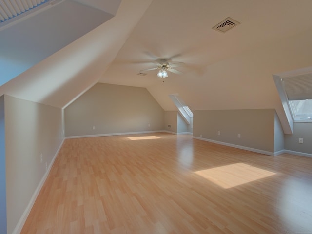 additional living space featuring light wood-type flooring, ceiling fan, and lofted ceiling with skylight