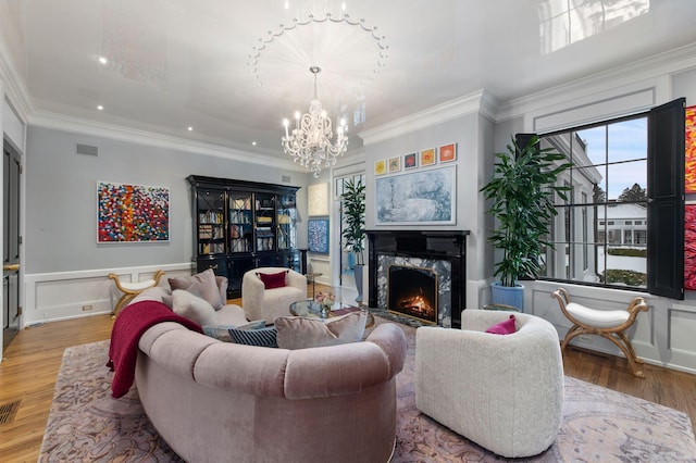 living room with an inviting chandelier, hardwood / wood-style floors, crown molding, and a high end fireplace