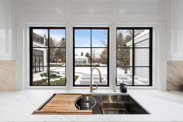 room details featuring sink, white cabinets, and light stone counters