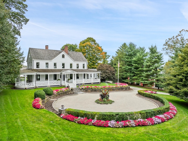 rear view of property featuring a porch, a lawn, curved driveway, and a chimney