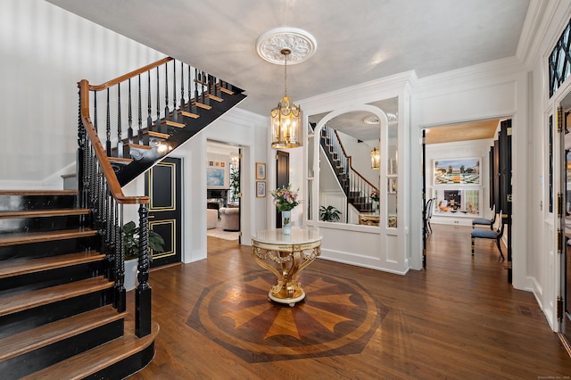 foyer entrance with crown molding, arched walkways, dark wood-style floors, and stairway