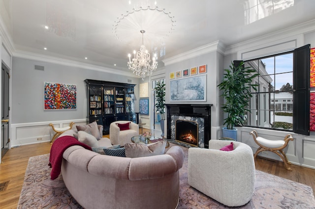 living area featuring a notable chandelier, a fireplace, wood finished floors, visible vents, and ornamental molding
