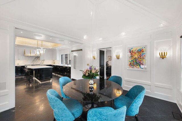 dining space featuring crown molding, marble finish floor, a decorative wall, and a notable chandelier