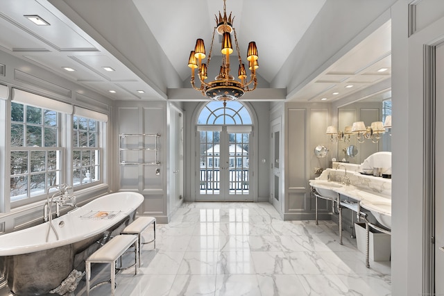 bathroom featuring an inviting chandelier, a freestanding bath, a decorative wall, french doors, and marble finish floor