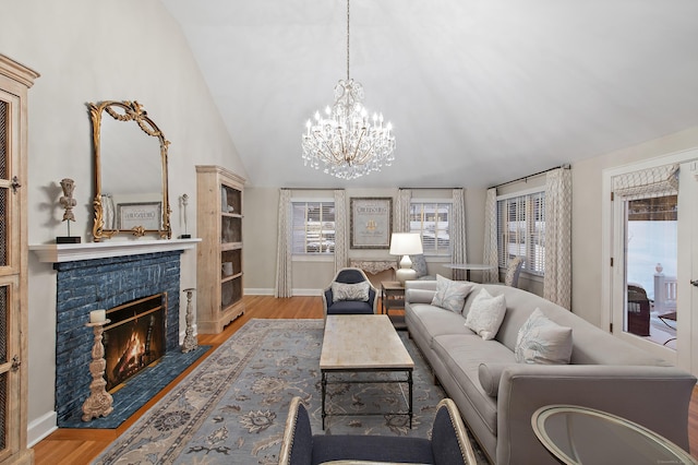 living area with an inviting chandelier, baseboards, a brick fireplace, and wood finished floors