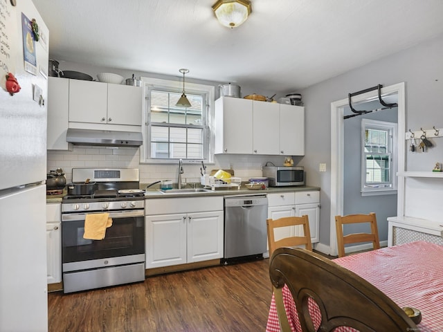 kitchen with sink, appliances with stainless steel finishes, pendant lighting, range hood, and white cabinets