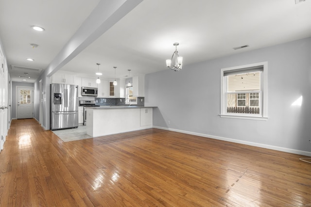 kitchen with white cabinetry, kitchen peninsula, appliances with stainless steel finishes, a chandelier, and pendant lighting