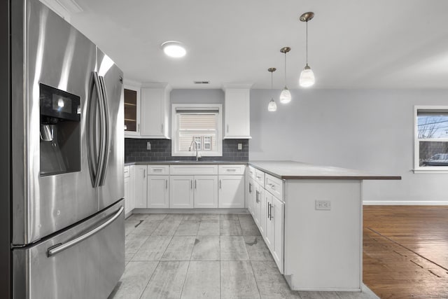 kitchen with white cabinetry, sink, hanging light fixtures, stainless steel fridge, and kitchen peninsula