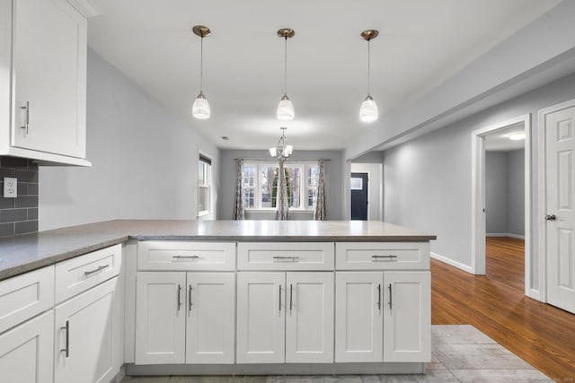 kitchen with decorative light fixtures, white cabinets, kitchen peninsula, and backsplash